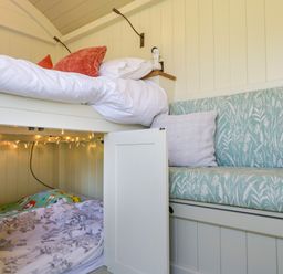 A bedroom with a bunk bed and a built-in cushioned seating area with pillows at Hazel in South Leigh near Witney