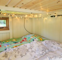 A small bed with colorful animal print bedding and floral duvet under wooden ceiling with string lights by a small window in Hazel South Leigh near Witney