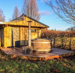 A wooden shed with a hot tub on a concrete platform in a grassy outdoor area at Cedrus Lodge in Skelton near Penrith