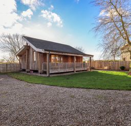 A wooden lodge with a covered porch surrounded by a gravel driveway and a grassy yard at Cedrus Lodge in Skelton near Penrith