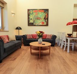 A living room with two dark sofas and a round wooden table with flowers and a dining table with white chairs at Cedrus Lodge in Skelton near Penrith