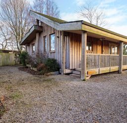 A wooden cabin with a gravel driveway and a porch at Larch Lodge in Skelton near Penrith