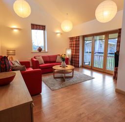 A living room with red sofas and a round wooden coffee table at Larch Lodge in Skelton near Penrith