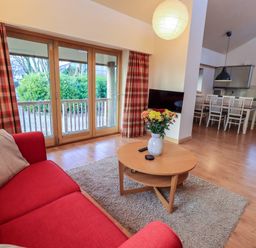A living room with red sofas a round wooden coffee table with flowers and a TV near dining area at Larch Lodge in Skelton near Penrith
