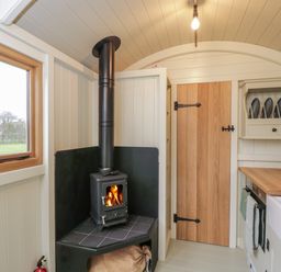 A small kitchen area with a wood burning stove a wooden door and a countertop with a sink at Spindle South Leigh near Witney
