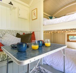 A small interior space with a table holding mugs and glasses of orange juice near cushioned bench seating and a bunk bed with string lights at Spindle in South Leigh near Witney