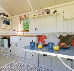 A kitchen area with a table set with drinks and pastries next to a cushioned bench with pillows at Spindle South Leigh near Witney