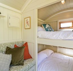A small bedroom with bunk beds and a cushioned bench seat with pillows at Spindle South Leigh near Witney