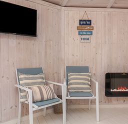 Two chairs with striped cushions a wall-mounted television a wall-mounted electric fireplace and wooden panel walls at Barley Bay near Hartland