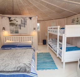 A bedroom with a double bed and bunk beds with blue striped bedding at Barley Bay near Hartland