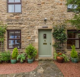 Exterior of a stone cottage with a green front door and potted plants at Crescent Cottage in Haltwhistle near Hadrians Wall