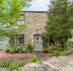 Exterior of a stone cottage with a green door and surrounding plants at Crescent Cottage in Haltwhistle near Hadrians Wall