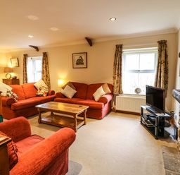 A living room with red sofas a wooden coffee table a TV on a stand and windows with patterned curtains at Crescent Cottage in Haltwhistle near Hadrians Wall