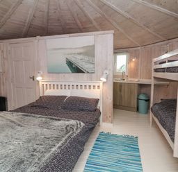 A bedroom with a double bed and bunk beds next to a small kitchen area at Spekes Mill near Hartland