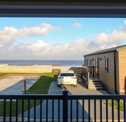 A view of a driveway with a white car parked next to a wooden lodge facing the sea at The Sea Lodge in Bacton near Walcott