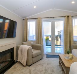 A living room with armchairs a coffee table a wall-mounted television and glass doors leading to a balcony at The Sea Lodge in Bacton near Walcott