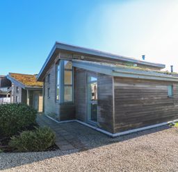 A wooden house with large windows and gravel pathway surrounded by shrubs at Una Lodge 77 in Carbis Bay