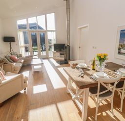 A living room with dining table set with plates and glasses and a sofa set near large windows at Una Lodge 77 in Carbis Bay