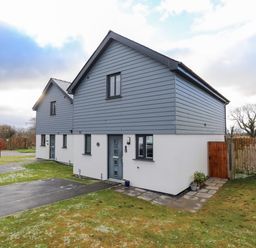 A two story house with gray siding and white walls next to a driveway and lawn at 19 Parc Delfryn in Benllech