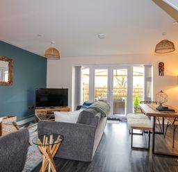A living room with a television sofa glass table and a dining table with chairs at 19 Parc Delfryn in Benllech