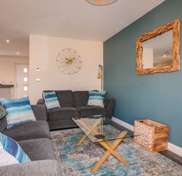 A living room with gray sofas blue and white pillows a glass coffee table a wall clock a wooden mirror and a decorative box at 19 Parc Delfryn in Benllech