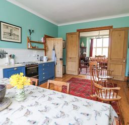 A kitchen with blue cabinets wooden chairs and table with flowers near a living room at Plas Pontfaen near Fishguard and Newport Pembrokeshire