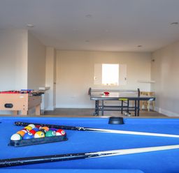 A game room with a blue pool table with balls and cues a foosball table and a ping pong table at Plas Gwylan in Rhosneigr