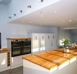 A kitchen with ovens refrigerators a wooden countertop island and a dining area with chairs at Plas Gwylan in Rhosneigr
