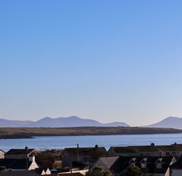 A coastal landscape with rooftops of houses in the foreground and a body of water with hills in the background at Plas Gwylan in Rhosneigr