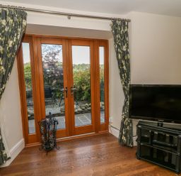 A room with wooden double doors leading outside floral curtains a television on a black stand and a bookshelf