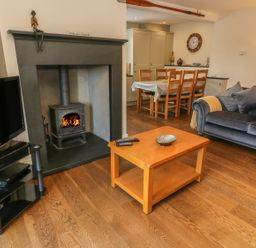 A living room with a wood burning stove television and dining table at Woodbine Cottage in Ambleside