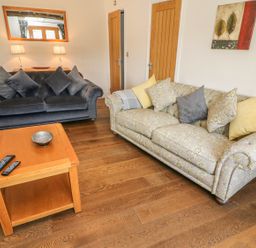 A living room with two sofas a wooden coffee table with remotes and a bowl a wall mirror and a painting at Woodbine Cottage in Ambleside