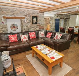 A living room with a leather sofa and Christmas cushions a wooden coffee table and a stone wall at Blacksmiths Cottage in Pembroke