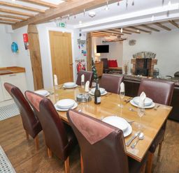 A dining area with a wooden table set for six and a kitchen area with white cabinets at Blacksmiths Cottage in Pembroke