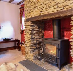 A room with a stone fireplace wood burning stove and a wooden table with a vase and a bowl at Old Farm Cottage in Woolacombe