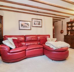 A living room with a red leather sectional sofa and framed pictures on the wall at Old Farm Cottage in Woolacombe
