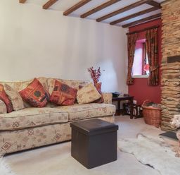 A living room with a patterned sofa red cushions stone fireplace and a dog on a rug at Old Farm Cottage in Woolacombe