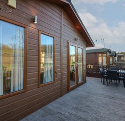 An outdoor deck area with a table and chairs attached to a wooden cabin at The Sanctuary Badgers Retreat Holiday Park near Catterick Garrison North Yorkshire