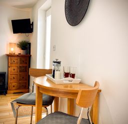 A small wooden dining table with two chairs and a tray with drinks next to a wooden cabinet and a wall-mounted TV at The Studio in Crackington Haven