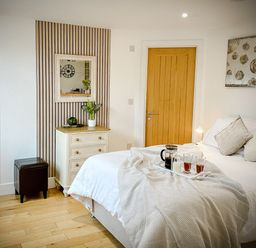 A bedroom with a bed and a tray on it a chest of drawers with a plant and mirror above and two wooden doors at The Studio in Crackington Haven