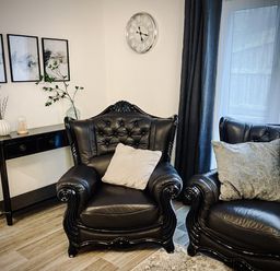 A living room with black leather armchairs and a black console table with vases near a window with dark curtains at Trelawne Near Crackington Haven