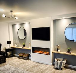 A living room with a black leather armchair shelves with decorative items a TV above a fireplace and two round mirrors at Trelawne Near Crackington Haven
