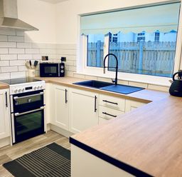 A kitchen with white cabinets wooden countertops a black sink a stove a microwave a kettle and a toaster at Trelawne Near Crackington Haven