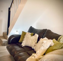 A living room with a dark leather sofa with cushions under a staircase at Penkenna in Crackington Haven