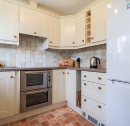 A kitchen with white cabinets a double oven a kettle on the counter and a white refrigerator at Bay Tree Cottage in Peasenhall