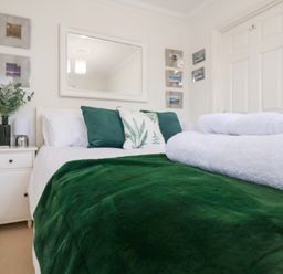 A bedroom with a bed covered with a green blanket and white towels on top at Bay Tree Cottage in Peasenhall
