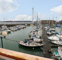 A marina with multiple moored sailboats and yachts and buildings in the background at 15 Sovereign House in Milford Haven