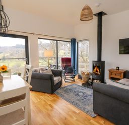 A living room with sofas a wood stove and large windows showing a landscape at Dundarach in Aberfeldy