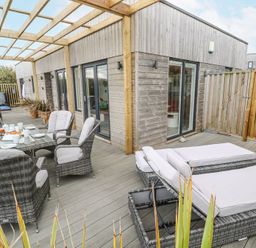 An outdoor patio with wicker chairs and loungers on a wooden deck at Petroc in Portreath