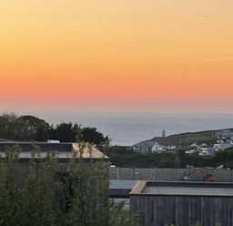 A sunset over the ocean with a coastal village and buildings in the foreground at Petroc in Portreath